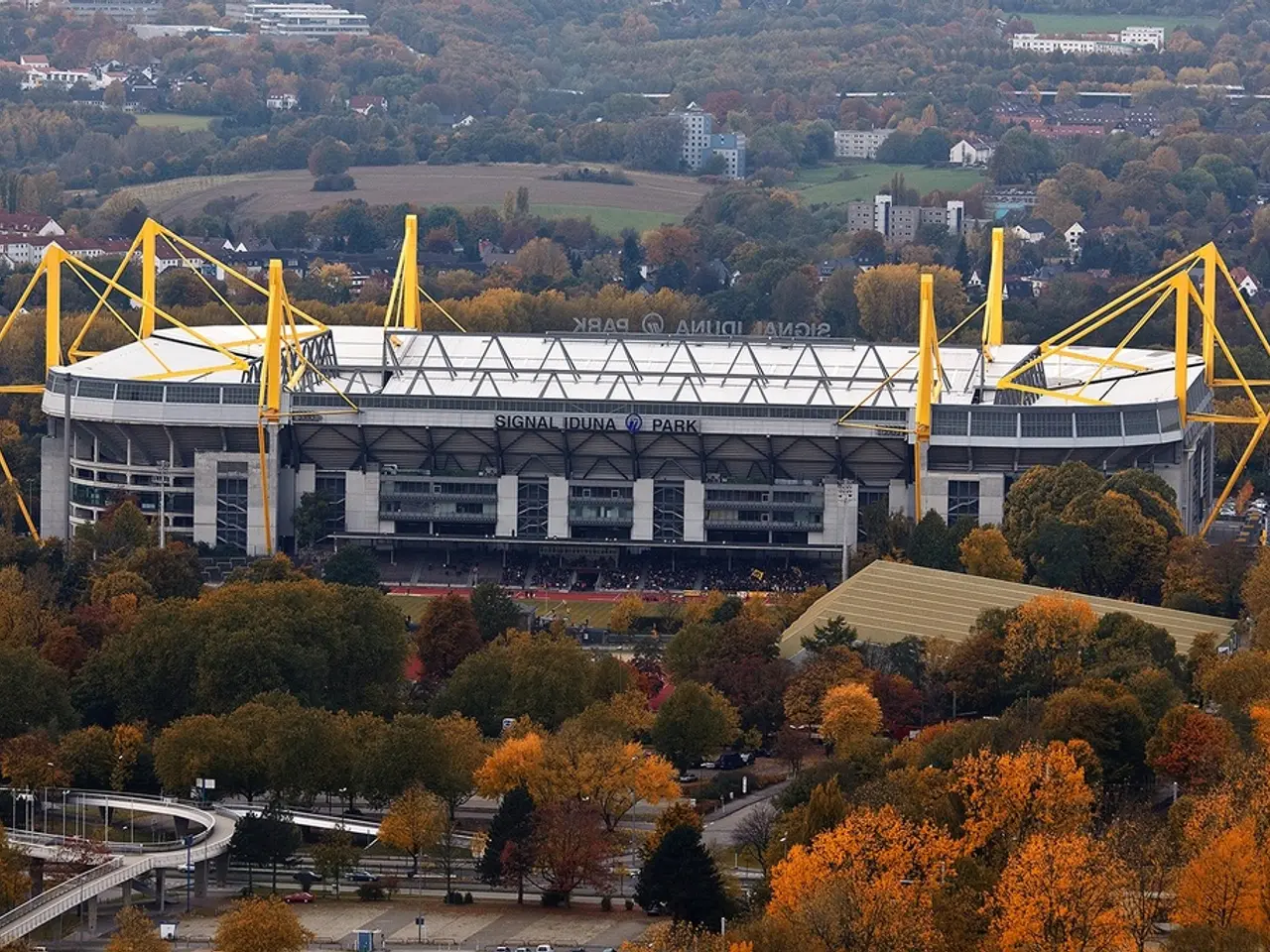 In the foreground of this image, there are many trees, fly over, road and vehicles moving on the...