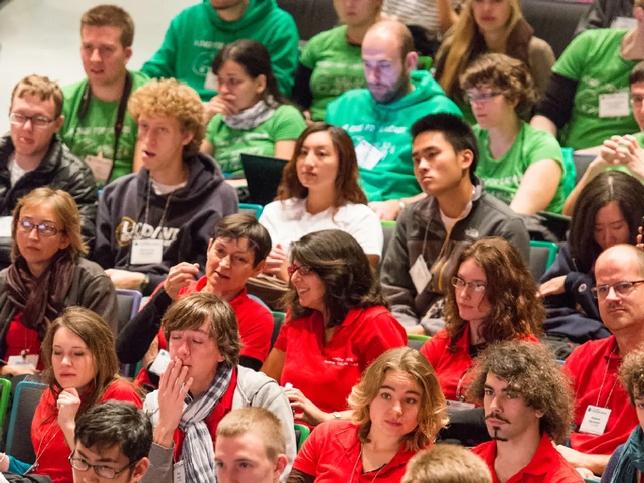 This image is taken indoors. In this image many people are sitting on the chairs and a few are...