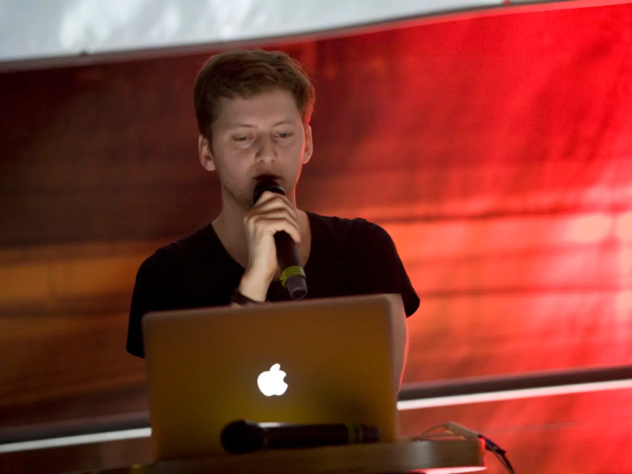 Here in the center we can see one person is holding microphone. In front of him there is a laptop....