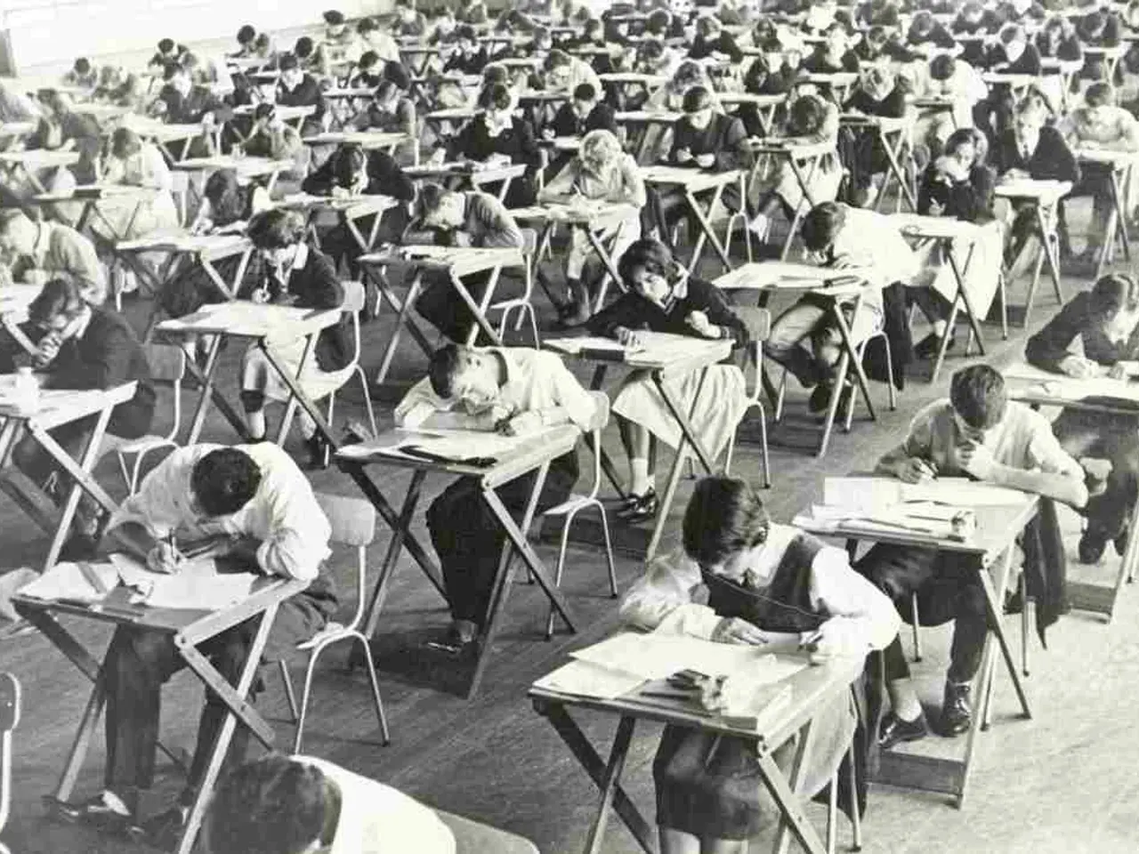 There are many people in this room, in the chairs and writing something on the tables on the...