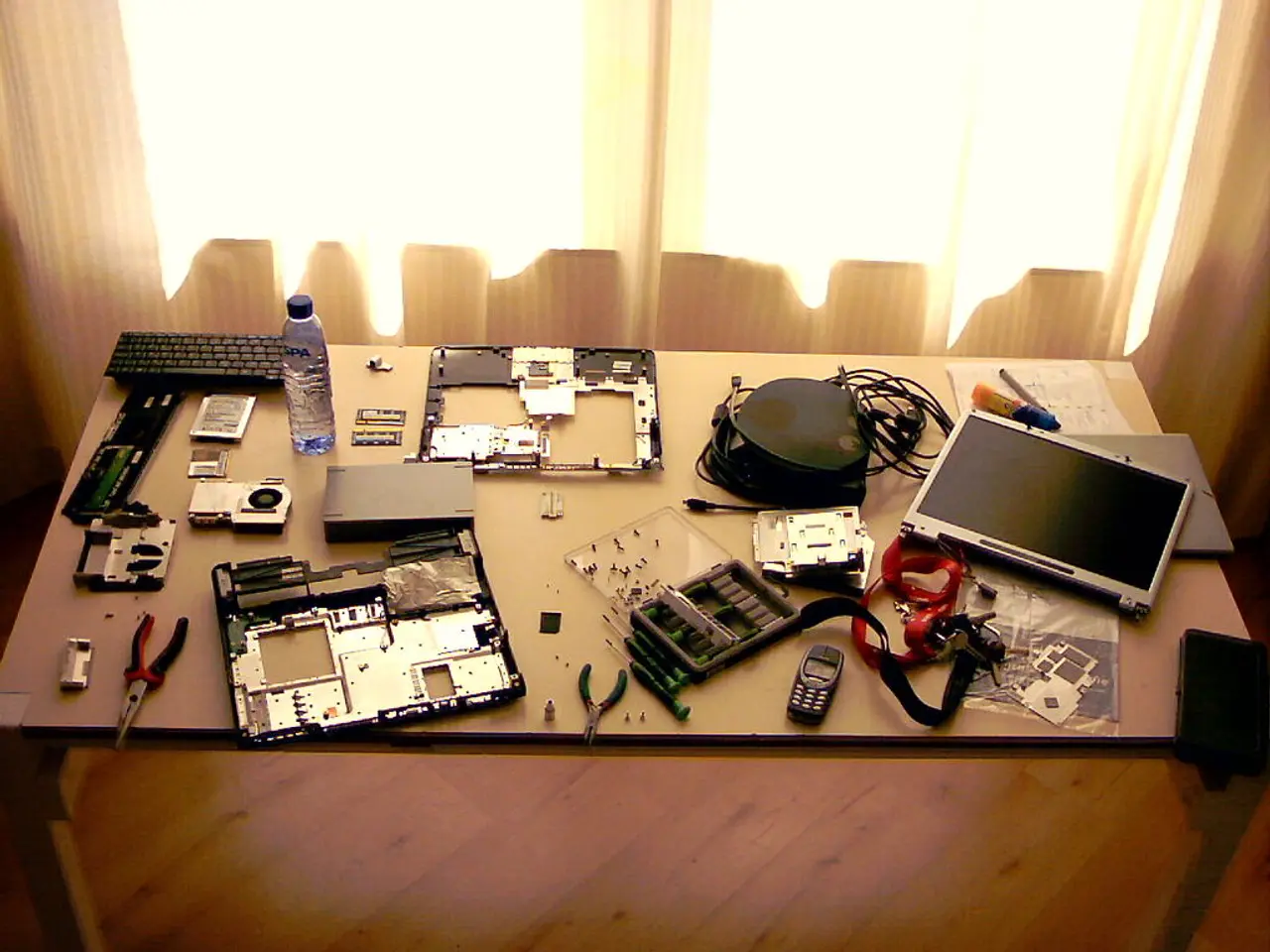 In this picture we can see table and on table we have keyboard, bottle, mobile, screwdriver, wires,...