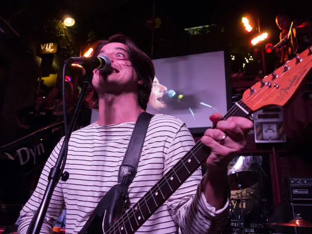 In this image i can see a man holding a guitar and singing song in front a micro phone at the back...