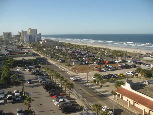 In this image there are vehicles and there are trees, buildings, and there is an ocean.